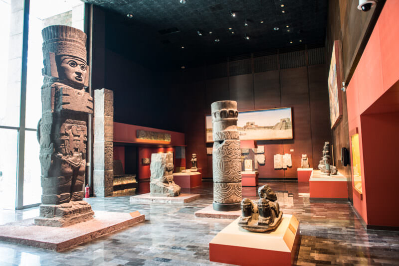 Full Toltec-style atlantean warrior column and decorated cylindrical pillars in Teotihuacan hall, monumental stone figures displayed