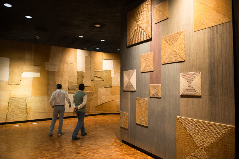 Wall-mounted woven textile panels filling two curving gallery walls in ethnography section