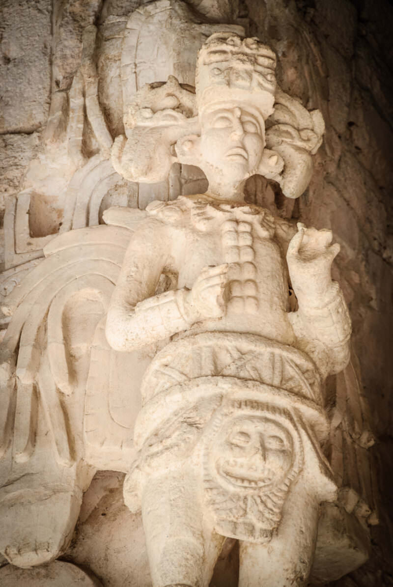Close-up of winged stucco figure from the Sak Xok Naah at Ek' Balam, showing elaborate headdress and beaded pectoral