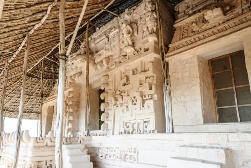 Sak Xok Naah façade under thatched palapa at Ek' Balam, displaying hieroglyphic scrollwork and ritual figures