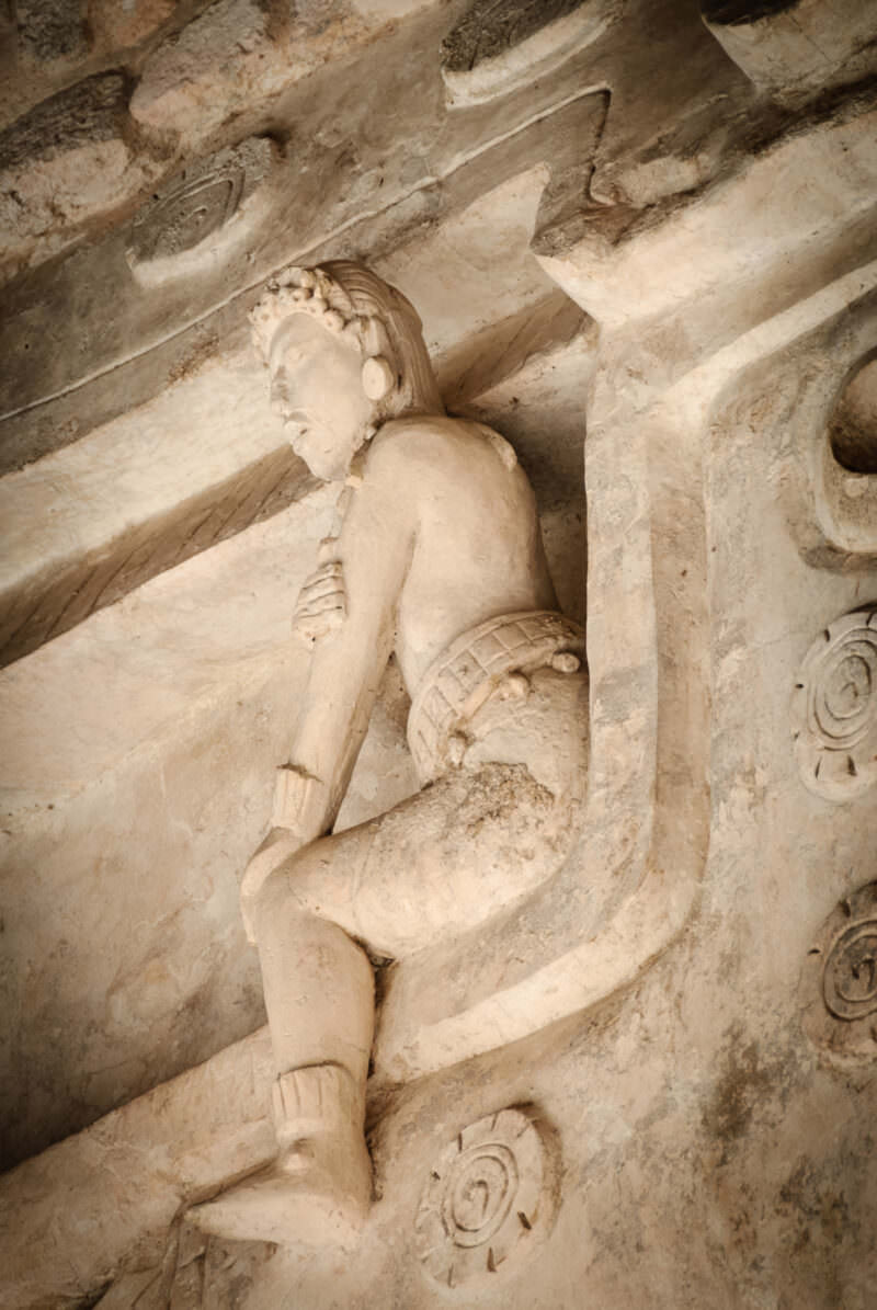 Smaller stucco figure reclining in a niche on the Sak Xok Naah façade at Ek' Balam, framed by scroll ornament