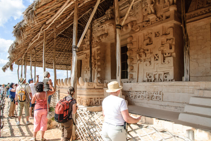 Tourists on the fourth-level terrace of Ek' Balam's Acropolis, photographing the Sak Xok Naah beneath its palapa roof