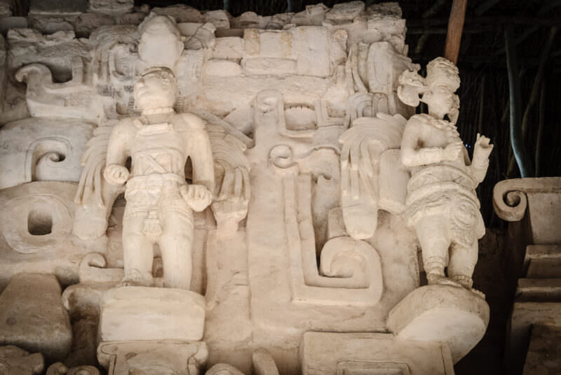 Two near-life-sized winged figures flanking the central serpent element of the Sak Xok Naah façade at Ek' Balam