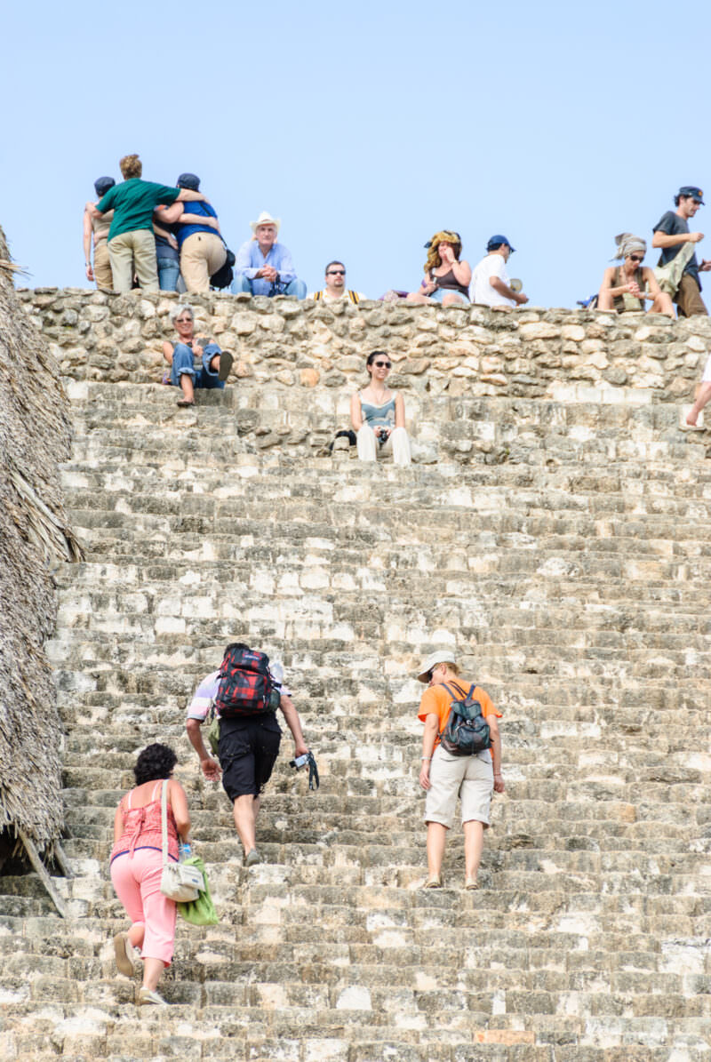 Visitors climbing and resting on the broad limestone terraces of Ek' Balam's Acropolis under a clear blue sky