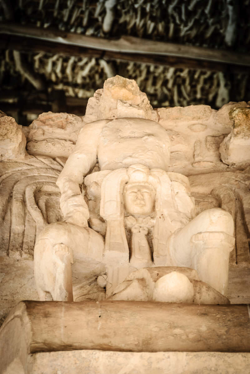 Seated winged figure from the Sak Xok Naah façade beneath the dense upper stucco frieze of Ek' Balam's Acropolis
