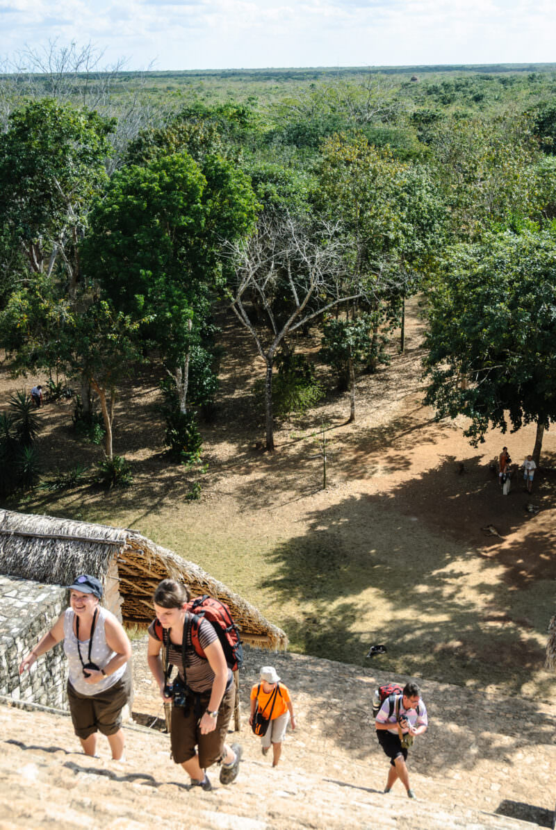 Visitors ascending the Acropolis staircase at Ek' Balam, with the flat Yucatán lowland forest stretching to the horizon
