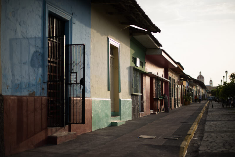 Calle La Calzada with pastel colonial facades, iron grilles, and the Cathedral of Granada dome in the distance