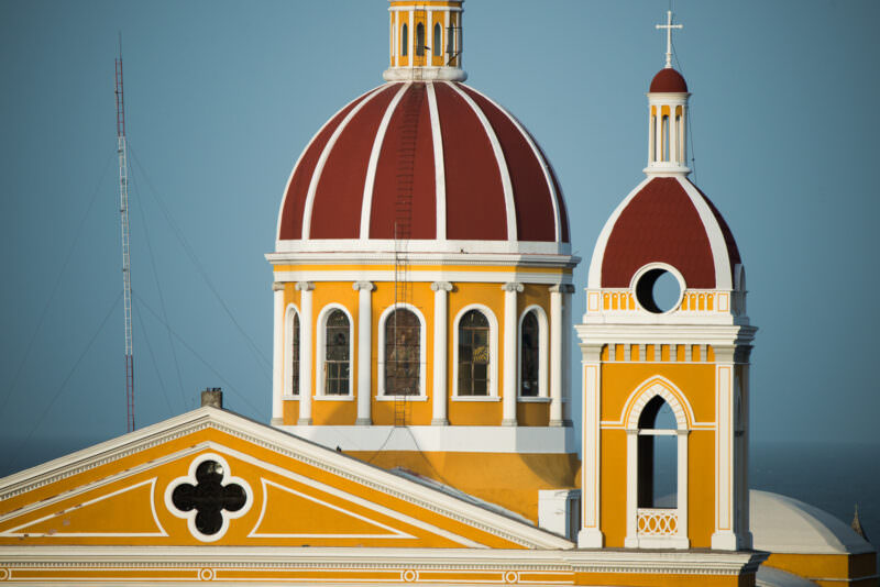 Cathedral of Granada's yellow facade with red-tiled dome and arched bell tower rising above Parque Central