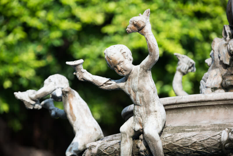 Weathered bronze putti holding shells on the central fountain pedestal in Parque Central