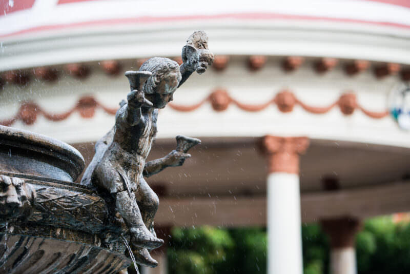 Bronze cherub on fountain in Granada's Parque Central, red-domed bandstand visible in soft focus behind