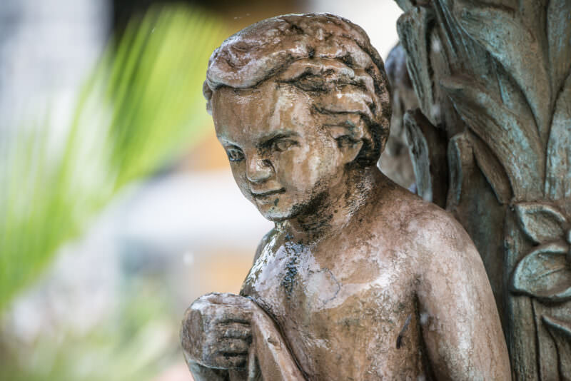 Weathered fountain sculpture of a boy in classical drapery, one arm raised, in Parque Central Granada