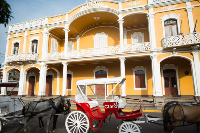 Brightly painted yellow horse-drawn carriage before yellow neoclassical facade with white columns and arches
