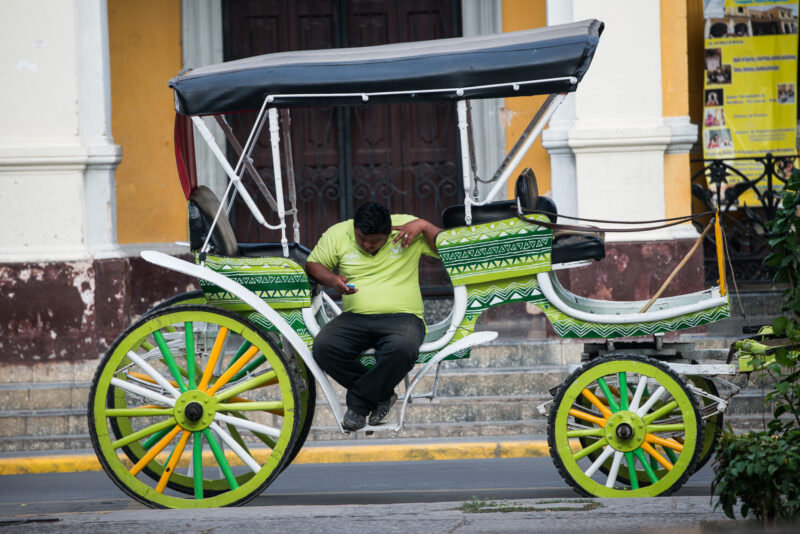 Carriage driver checking his phone in a lime-green painted horse-drawn carriage with geometric patterns at Parque Central