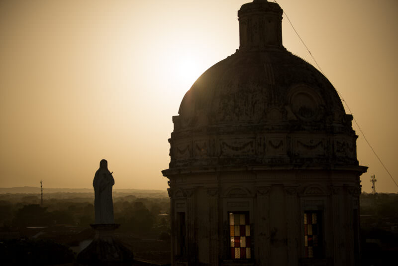 Silhouetted baroque dome and rooftop statue of Iglesia de la Merced at sunset with golden sky