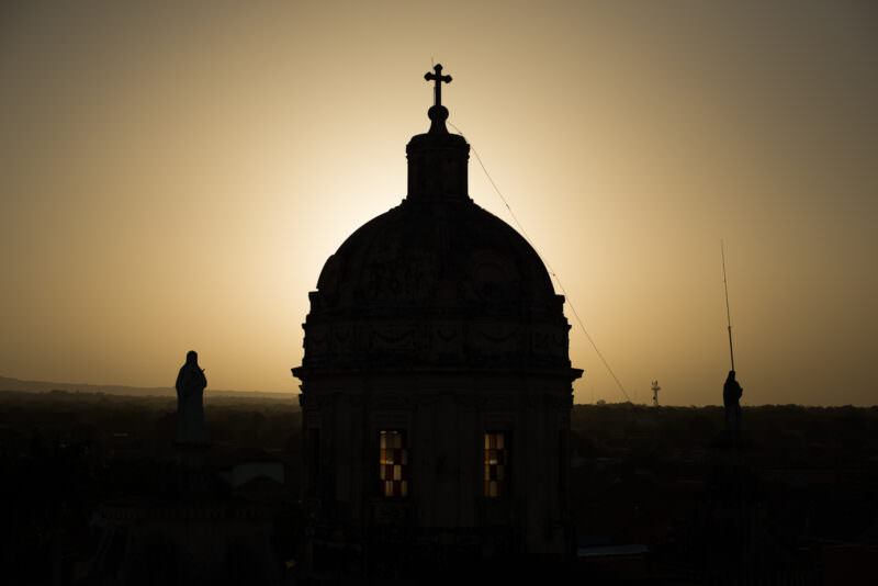 Silhouetted baroque dome of Iglesia de la Merced with sunlight piercing drum windows, viewed from the bell tower