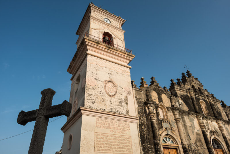 Iglesia de la Merced's baroque bell tower and facade with a carved stone cross in the foreground