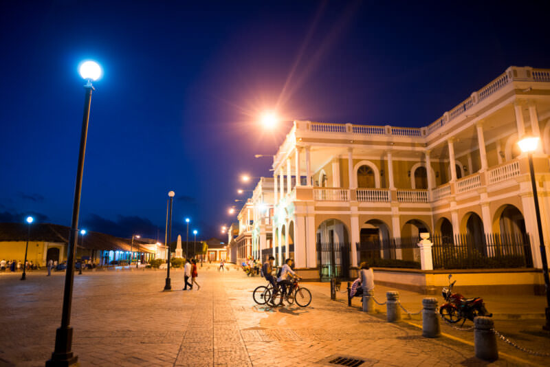 Night view of Independence Plaza in Granada showing illuminated neoclassical arcaded buildings and streetlamps