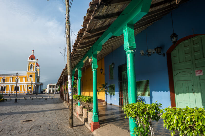 Bright green wooden pillars supporting portico with terracotta roof, yellow Granada Cathedral facade beyond