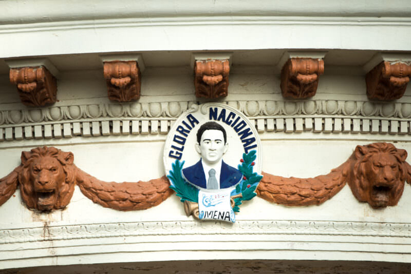 Painted relief medallion of José de la Cruz Mena flanked by lion heads on bandstand roofline