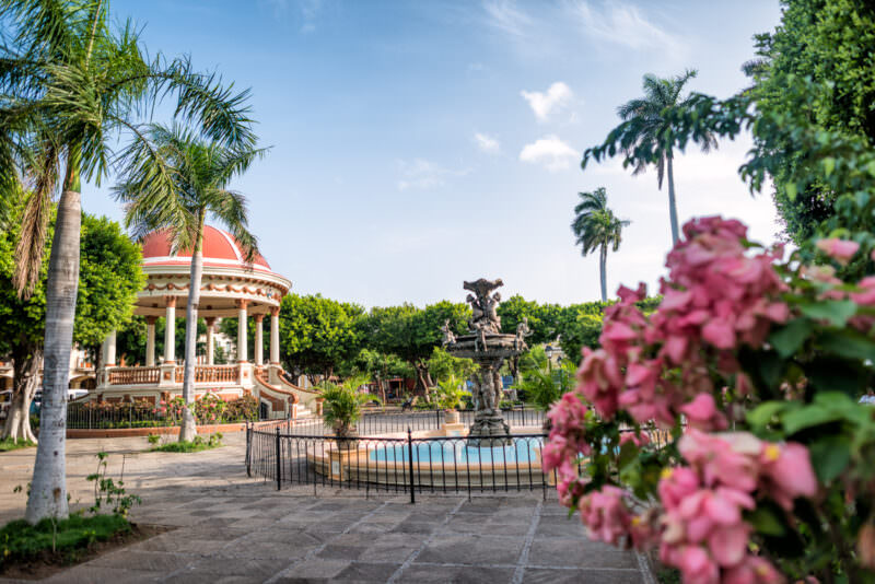 Tiered fountain and red-domed bandstand framed by pink bougainvillea in Parque Central Granada