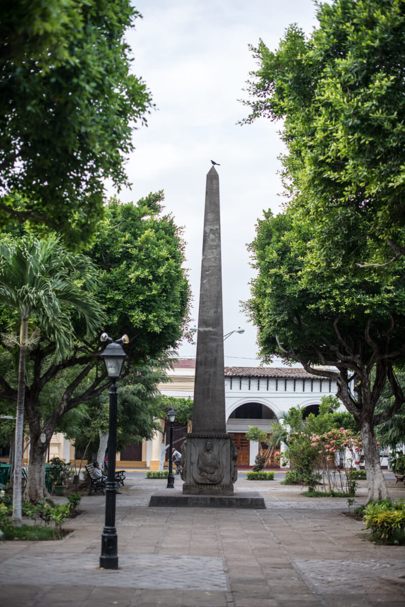 Rubén Darío Obelisk rising among trees in Parque Central, a bird perched at its peak
