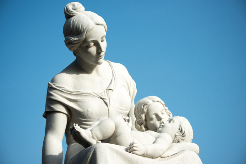White marble statue of mother cradling two children against blue sky in Parque Central
