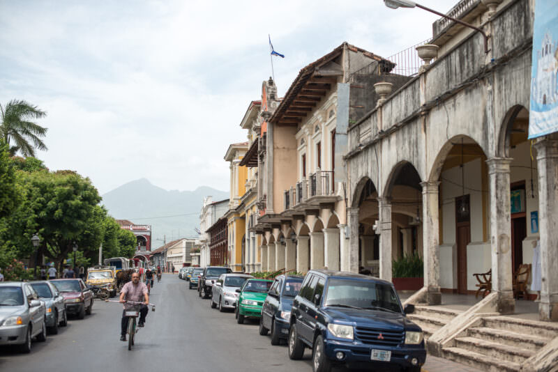 Arched colonnade along Parque Central in Granada framing distant volcanic peaks under cloudy sky