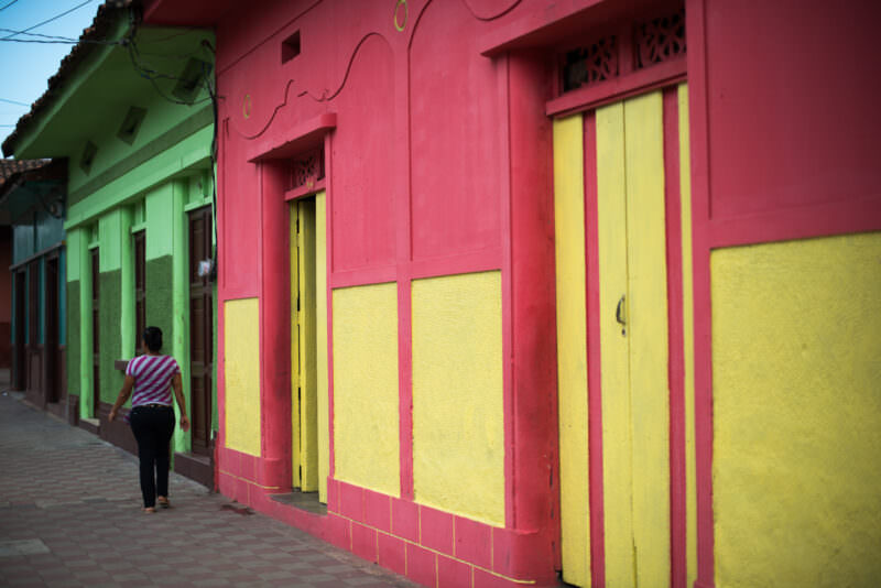 Pedestrian walking past pink and yellow colonial facades with tall wooden doors in Granada's historic center