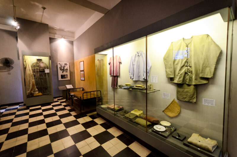 Glass display cases of American POW clothing, bedding and dishware in a Hoa Lo Prison exhibit