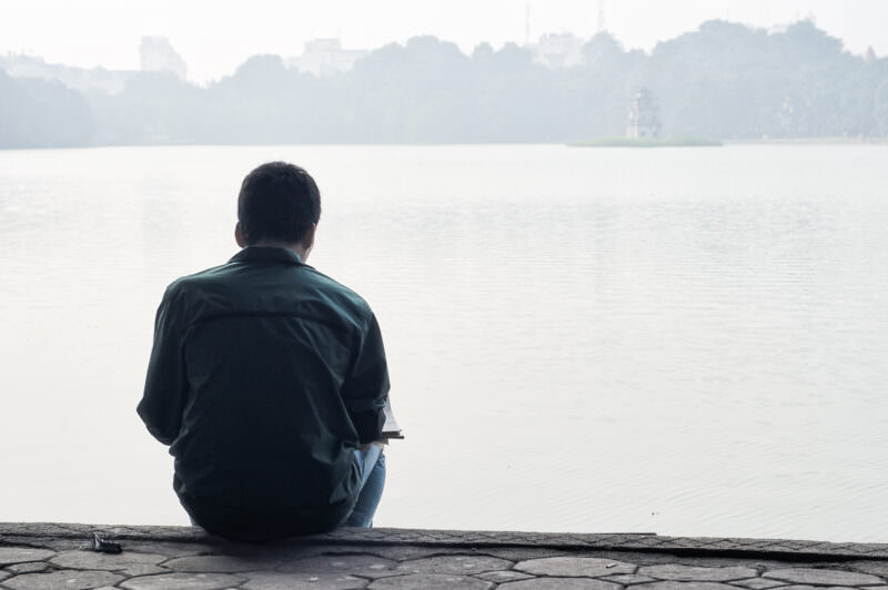 Man sketching by Hoan Kiem Lake with the fog-shrouded Turtle Tower silhouetted in the distance