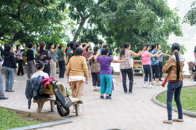 Women performing synchronized duong sinh exercises along the tree-lined promenade of Hoan Kiem Lake