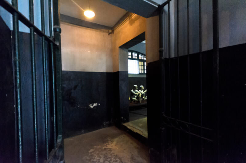 Iron gates opening onto mannequins on communal platforms in a Hoa Lo Prison cell block