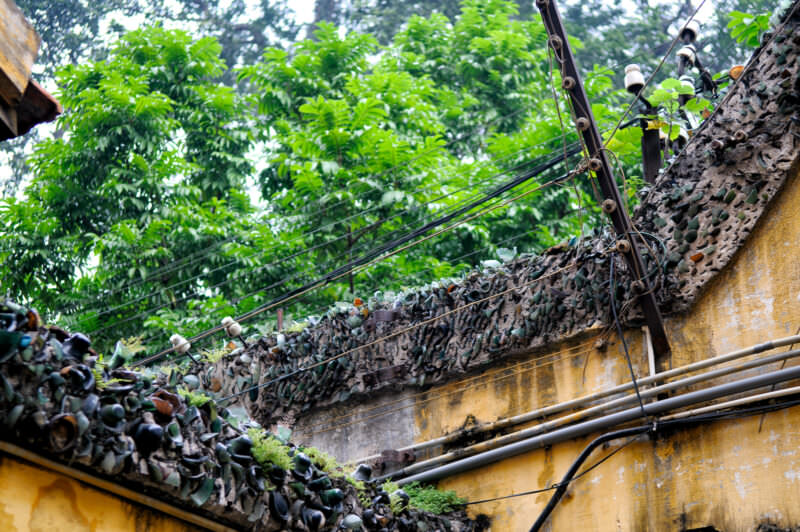 Broken glass shards and wire embedded atop the weathered perimeter wall of Hoa Lo Prison