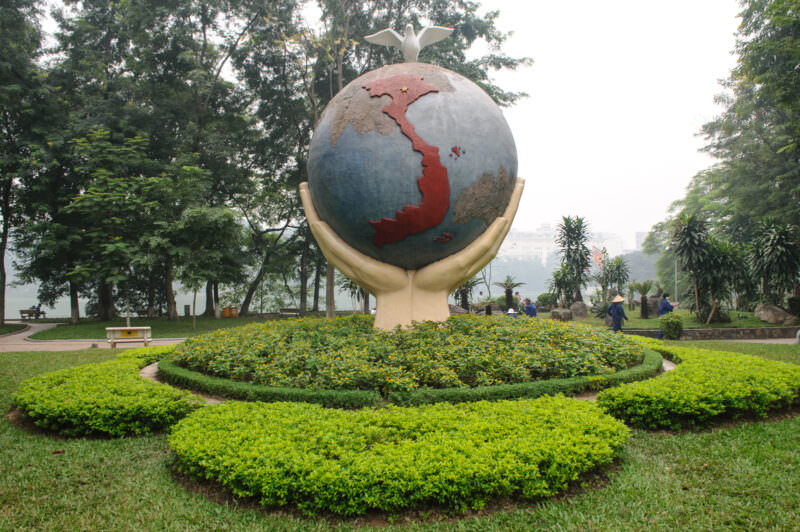 Hands cradling a globe sculpture with a Vietnam map and dove beside Hoan Kiem Lake