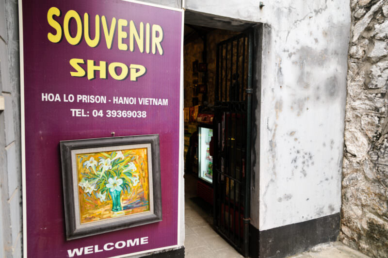 Purple souvenir shop sign beside an iron-barred entrance at Hoa Lo Prison