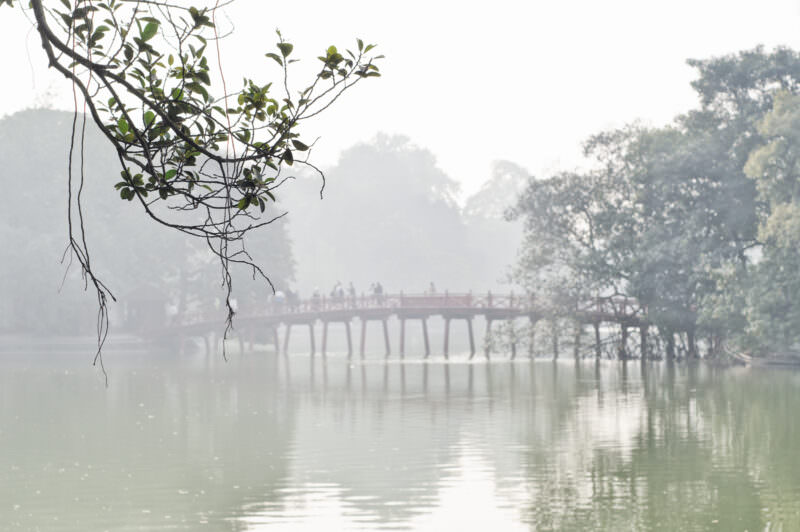 The Huc Bridge crossing misty Hoan Kiem Lake toward tree-hidden Ngoc Son Temple