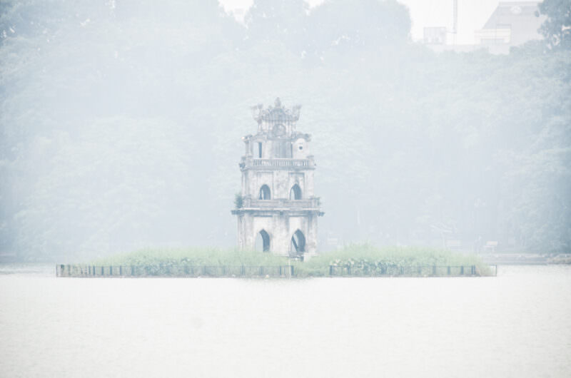 Turtle Tower's Gothic-arched silhouette emerging from dense morning fog over Hoan Kiem Lake