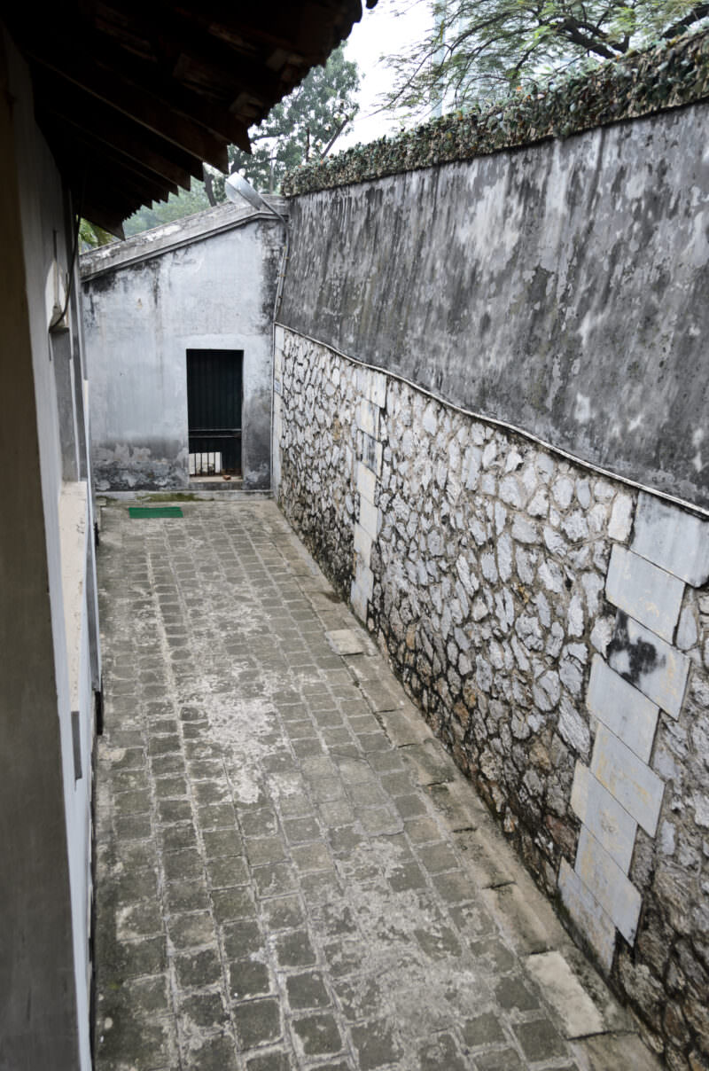 Cobblestone pathway running beside the tall stone perimeter walls of Hoa Lo Prison