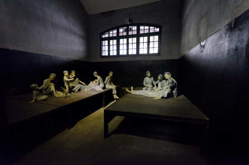 Sculpted figures recreating female political prisoners on wooden platforms at Hoa Lo Prison