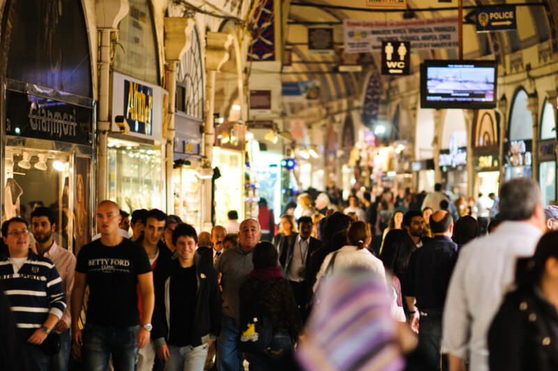 Crowded covered corridor of the Grand Bazaar with shoppers passing storefronts and overhead signage