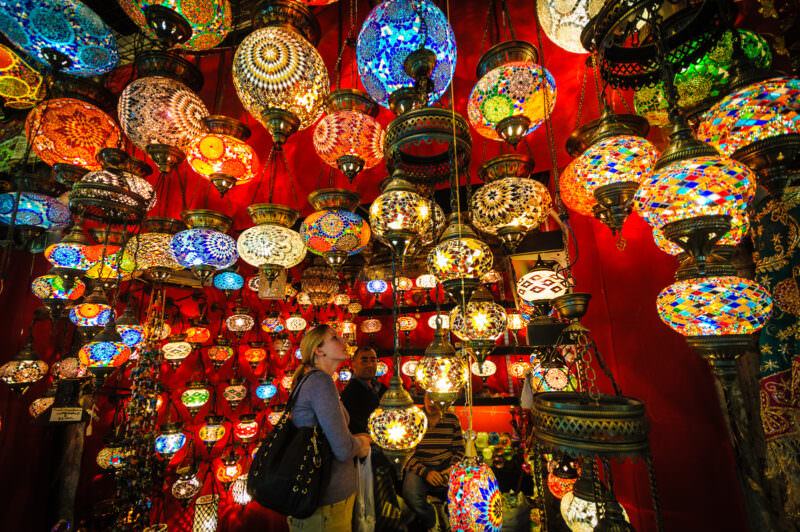 Woman browsing a shop crowded floor to ceiling with colorful mosaic glass lamps in the Grand Bazaar
