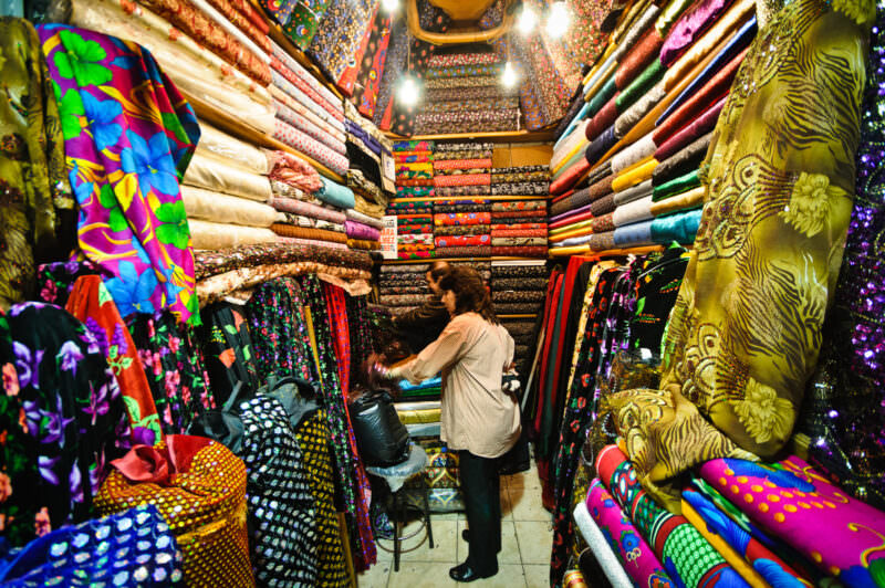 Woman shopping in a narrow Grand Bazaar textile stall stacked floor to ceiling with patterned fabric bolts