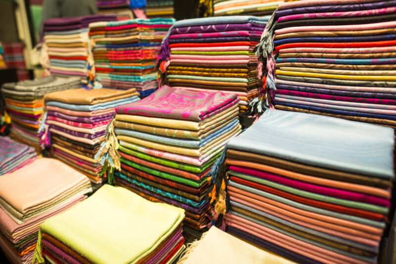 Neatly folded stacks of cashmere and silk scarves in varied colors at a Grand Bazaar textile stall