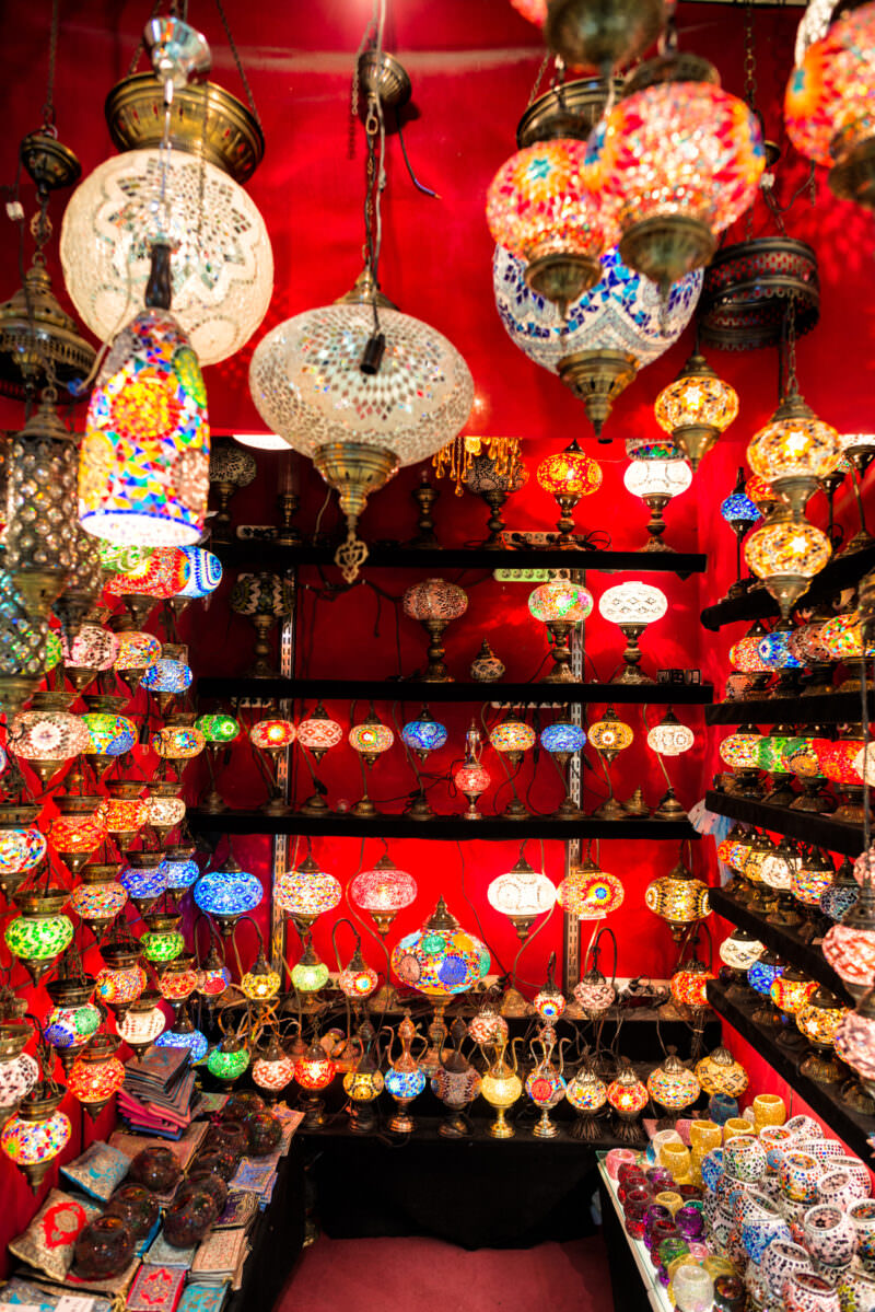 Close view of a Grand Bazaar shop stall packed with hanging and shelved mosaic glass lamps against a red wall