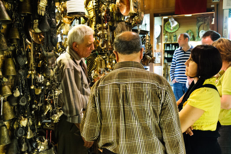 Shoppers haggling with a merchant surrounded by brass lanterns and antique wares in the Grand Bazaar