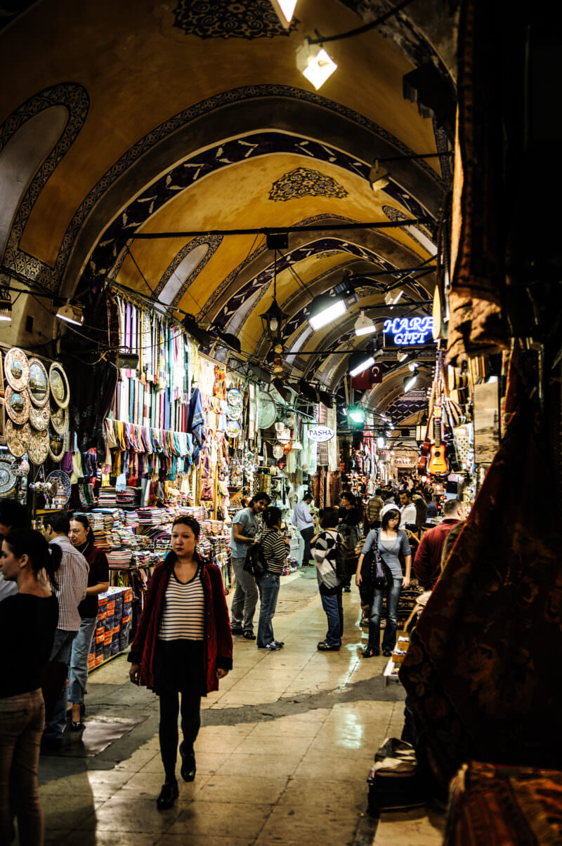 Woman walking beneath a painted stone vault along a covered street of the Grand Bazaar lined with shops