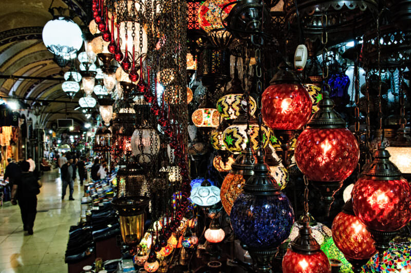 Teardrop mosaic glass lamps hanging above a Grand Bazaar shop lane, casting colored light across the passage