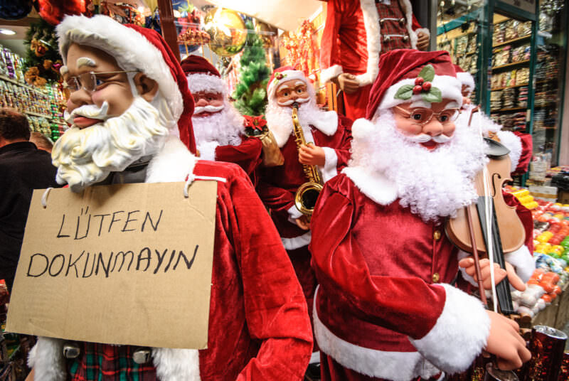 Santa Claus mannequins and a handwritten sign crowd a holiday shop window at the edge of the Grand Bazaar