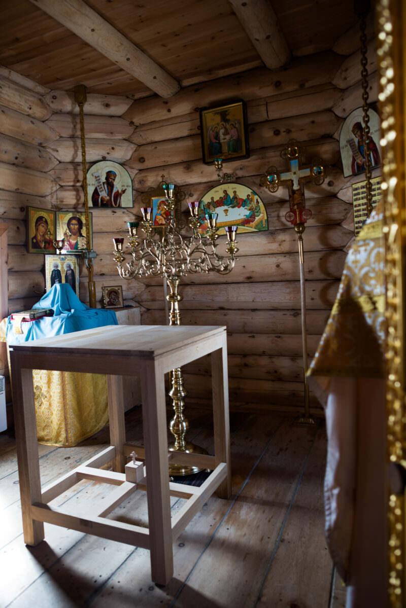 Warm timber interior with icon-lined walls and gilded iconostasis inside Trinity Church, King George Island