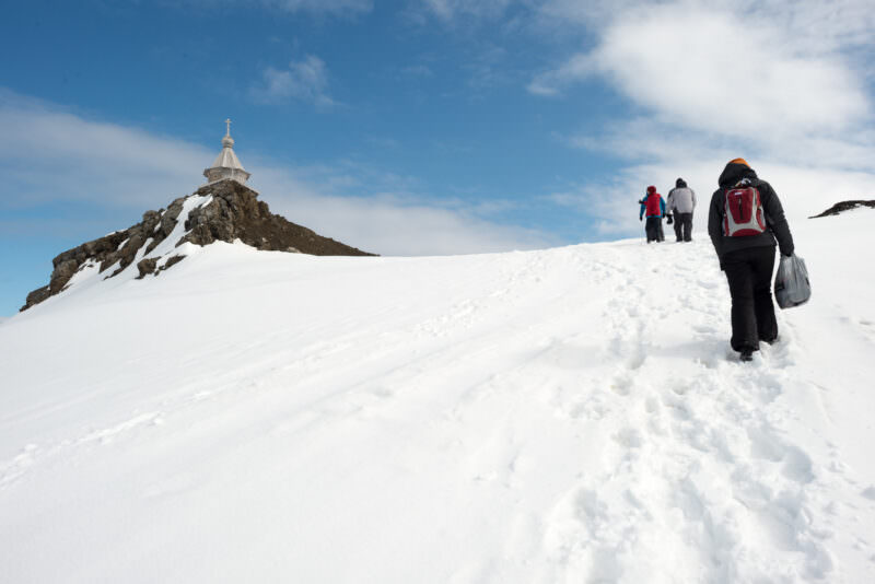 Visitors climbing steep snowy slope toward Trinity Church above Bellingshausen Station, King George Island